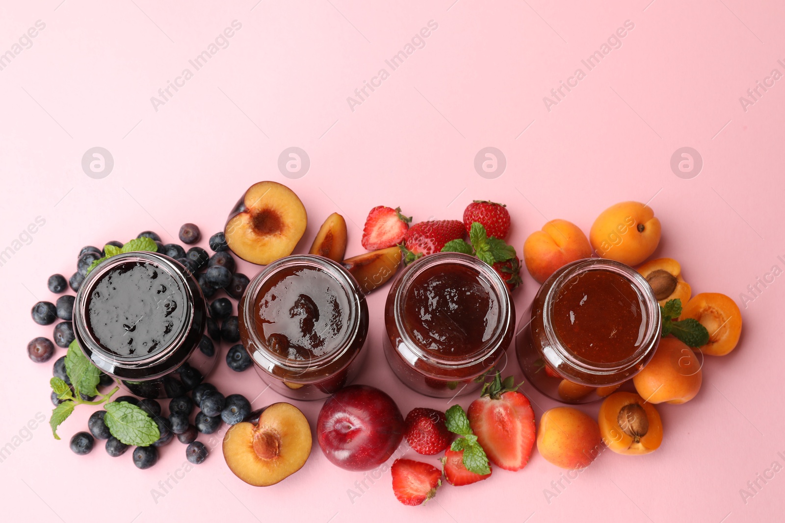 Photo of Different jams in jars and ingredients on light pink background, flat lay. Space for text