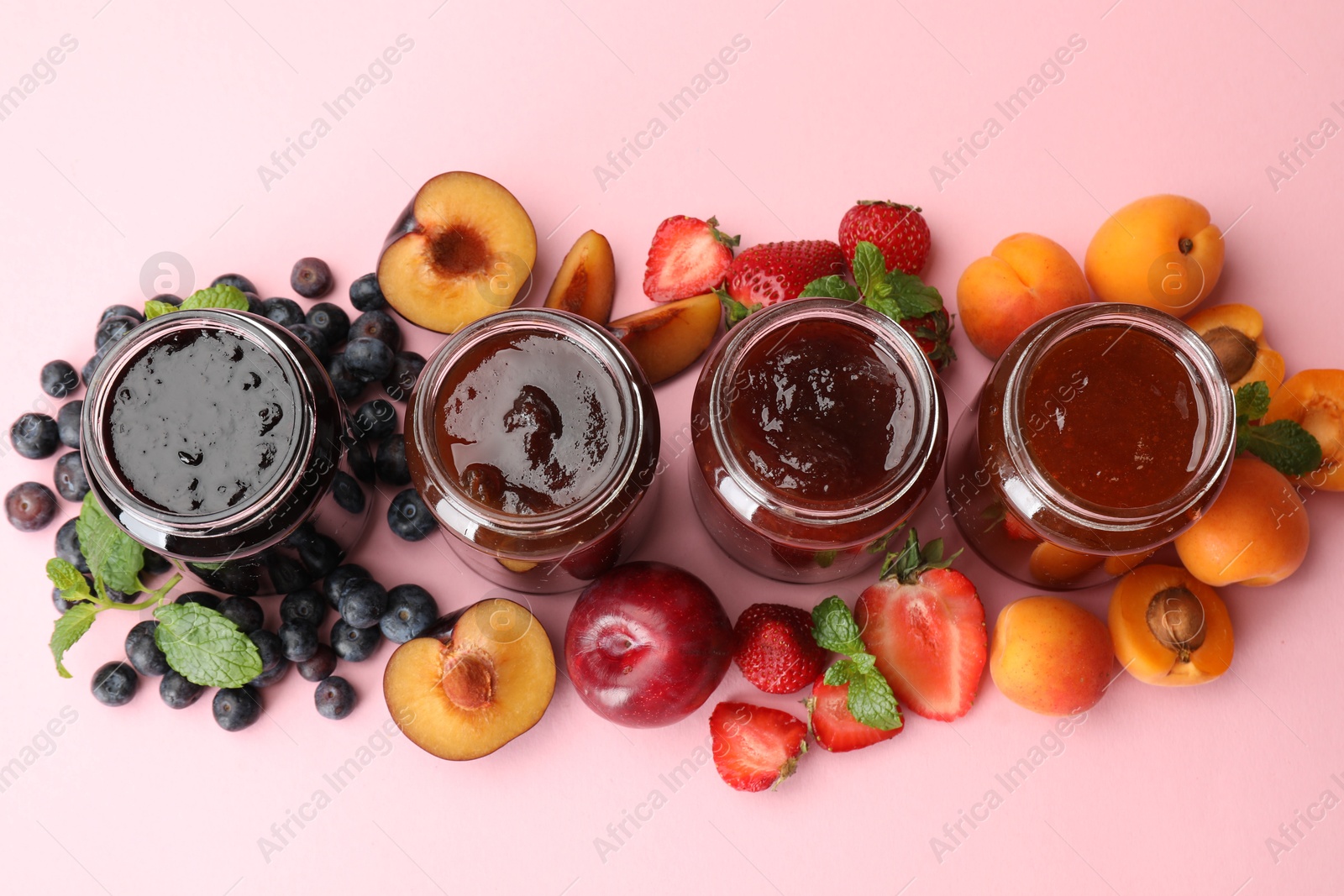 Different jams in jars and ingredients on light pink background, flat lay Photo of Different jams in jars and ingredients on light pink background, flat lay
