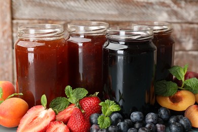 Photo of Different jams in jars and ingredients against wooden background, closeup