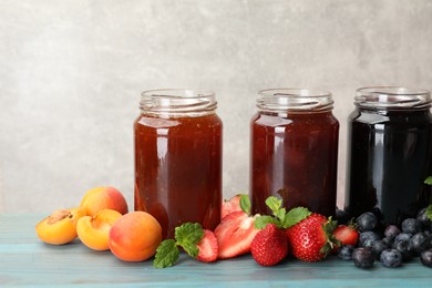 Photo of Different jams in jars and ingredients on blue wooden table. Space for text