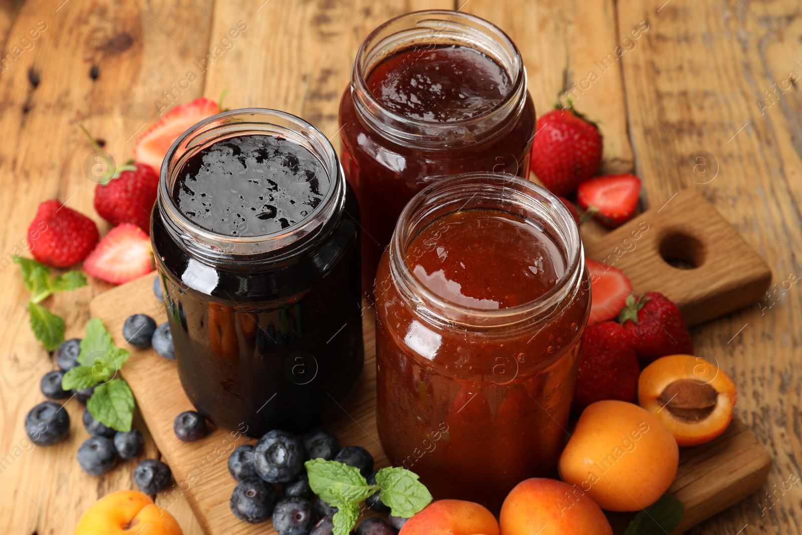 Different jams in jars and ingredients on wooden table, closeup Photo of Different jams in jars and ingredients on wooden table, closeup