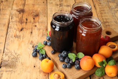 Photo of Different jams in jars and ingredients on wooden table. Space for text