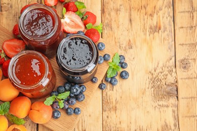 Photo of Different jams in jars and ingredients on wooden table, flat lay. Space for text
