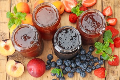 Photo of Different jams in jars and ingredients on wooden table, flat lay