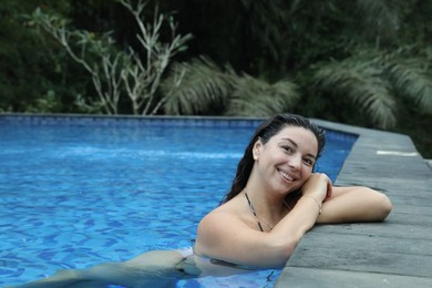 Photo of Happy woman relaxing in swimming pool outdoors, space for text