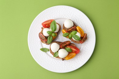 Photo of Tasty sandwiches with mozzarella cheese, tomatoes and basil on green background, top view
