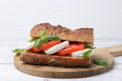 Photo of Tasty sandwich with mozzarella cheese, tomatoes and basil on white wooden table, closeup