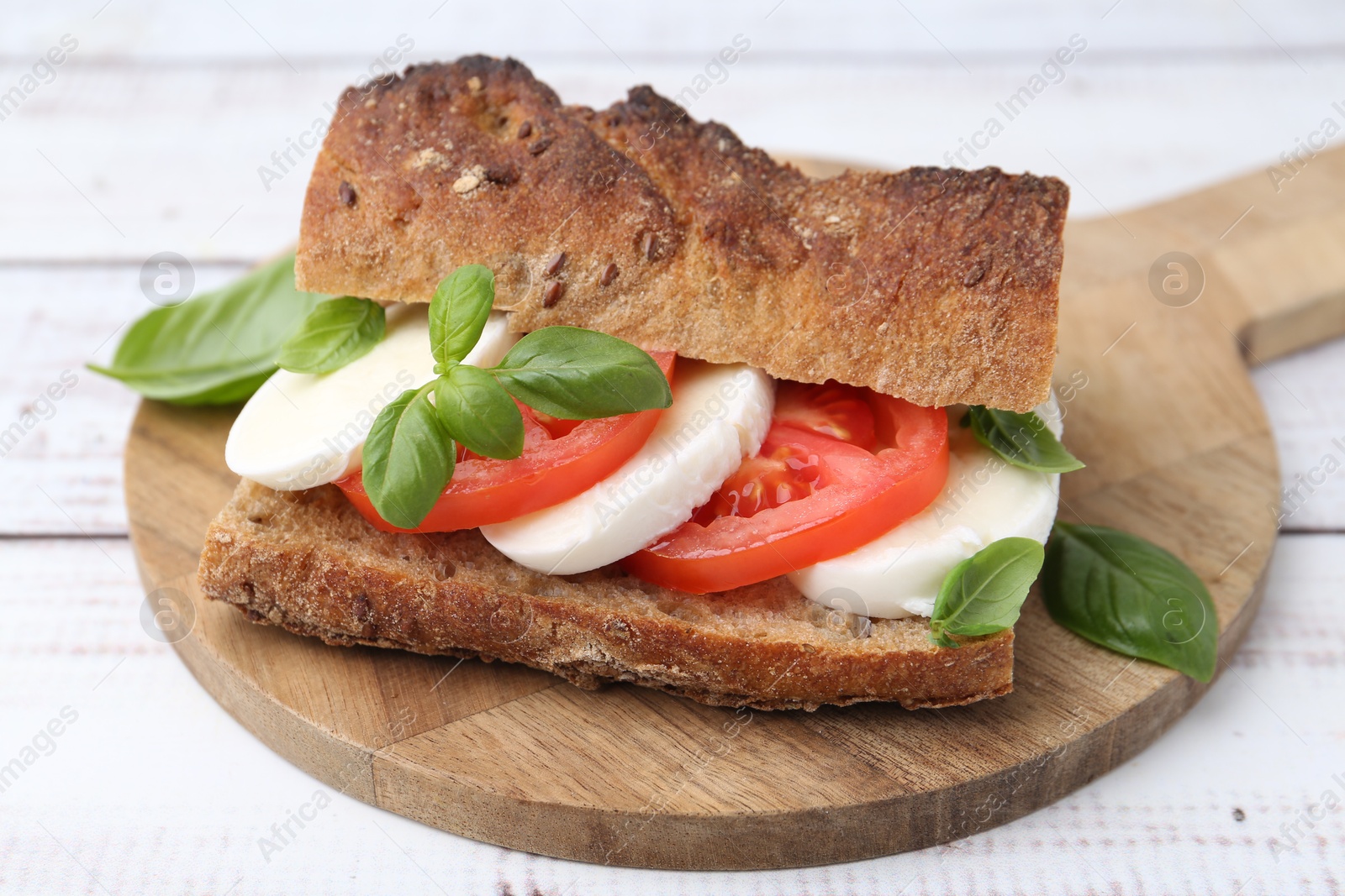 Tasty sandwich with mozzarella cheese, tomatoes and basil on white wooden table, closeup Photo of Tasty sandwich with mozzarella cheese, tomatoes and basil on white wooden table, closeup