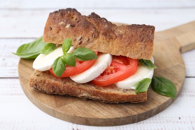 Photo of Tasty sandwich with mozzarella cheese, tomatoes and basil on white wooden table, closeup