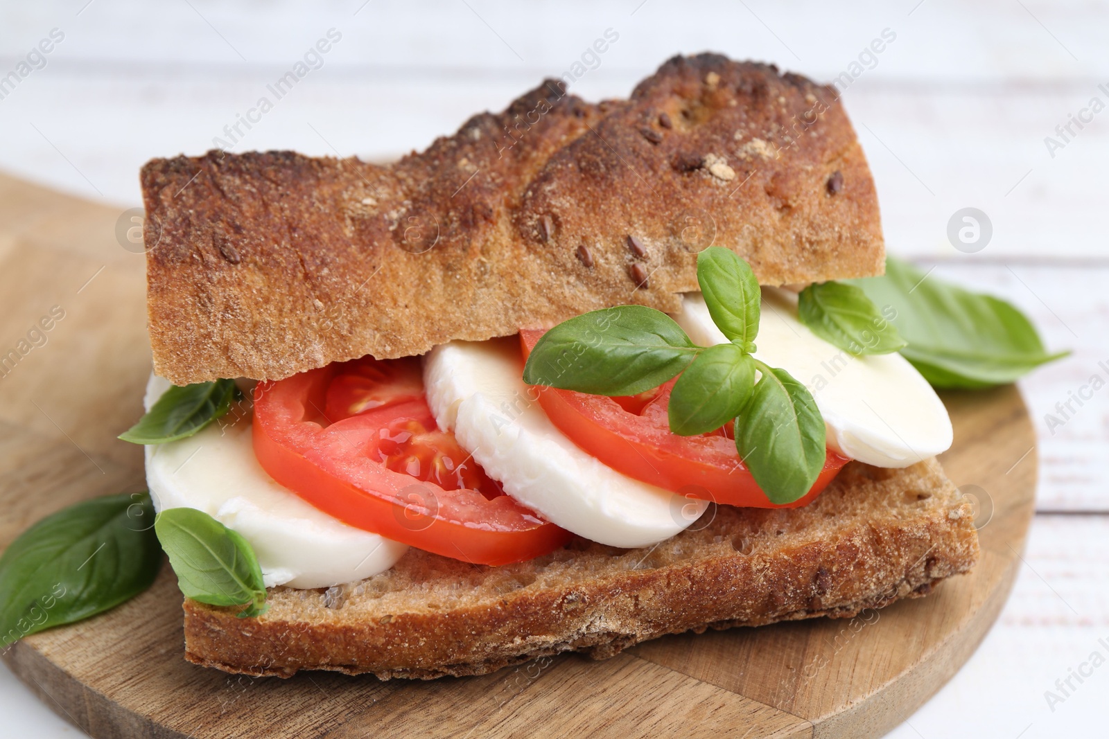 Tasty sandwich with mozzarella cheese, tomatoes and basil on white wooden table, closeup Photo of Tasty sandwich with mozzarella cheese, tomatoes and basil on white wooden table, closeup
