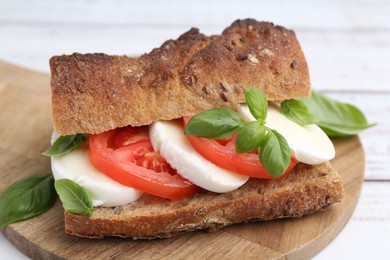 Photo of Tasty sandwich with mozzarella cheese, tomatoes and basil on white wooden table, closeup