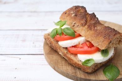 Photo of Tasty sandwich with mozzarella cheese, tomatoes and basil on white wooden table, closeup. Space for text