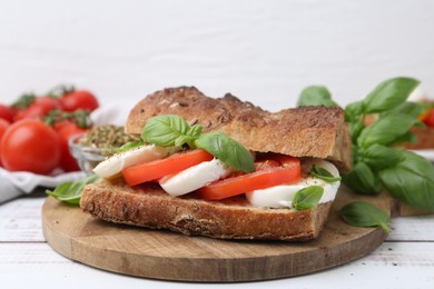 Photo of Tasty sandwich with mozzarella cheese, tomatoes and basil on white wooden table, closeup