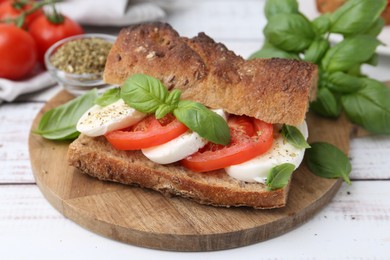 Photo of Tasty sandwich with mozzarella cheese, tomatoes and basil on white wooden table, closeup
