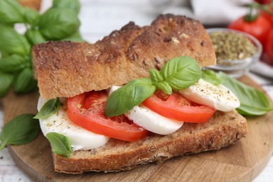 Photo of Tasty sandwich with mozzarella cheese, tomatoes and basil on white wooden table, closeup