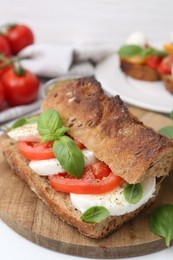Photo of Tasty sandwich with mozzarella cheese, tomatoes and basil on white wooden table, closeup