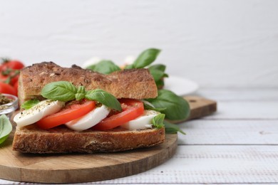 Photo of Tasty sandwich with mozzarella cheese, tomatoes and basil on white wooden table, closeup. Space for text