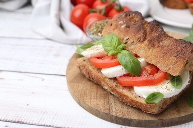 Photo of Tasty sandwich with mozzarella cheese, tomatoes and basil on white wooden table, closeup. Space for text