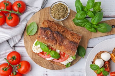 Photo of Tasty sandwich with mozzarella cheese, tomatoes and basil on white wooden table, flat lay