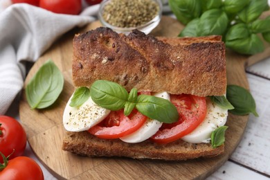 Photo of Tasty sandwich with mozzarella cheese, tomatoes and basil on white wooden table, closeup
