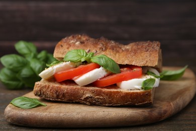 Photo of Tasty sandwich with mozzarella cheese, tomatoes and basil on wooden table, closeup