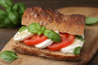 Photo of Tasty sandwich with mozzarella cheese, tomatoes and basil on wooden table, closeup