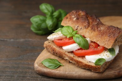 Photo of Tasty sandwich with mozzarella cheese, tomatoes and basil on wooden table, closeup. Space for text