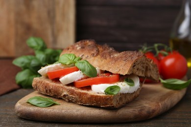 Photo of Tasty sandwich with mozzarella cheese, tomatoes and basil on wooden table, closeup