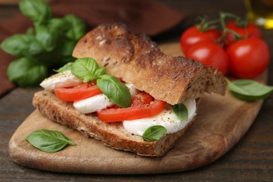 Photo of Tasty sandwich with mozzarella cheese, tomatoes and basil on wooden table, closeup