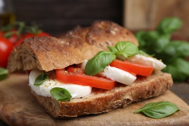 Photo of Tasty sandwich with mozzarella cheese, tomatoes and basil on wooden table, closeup