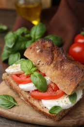 Photo of Tasty sandwich with mozzarella cheese, tomatoes and basil on wooden table, closeup