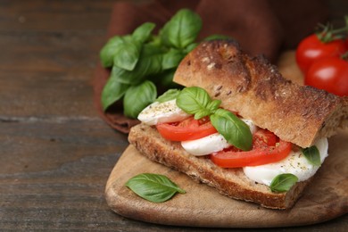 Photo of Tasty sandwich with mozzarella cheese, tomatoes and basil on wooden table, closeup. Space for text