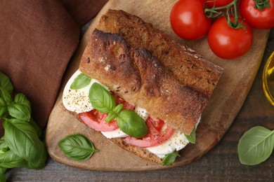 Photo of Tasty sandwich with mozzarella cheese, tomatoes and basil on wooden table, flat lay