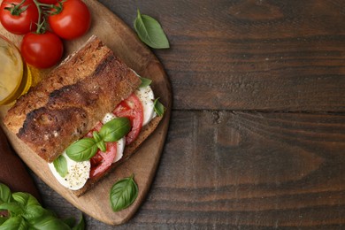 Photo of Tasty sandwich with mozzarella cheese, tomatoes and basil on wooden table, flat lay. Space for text