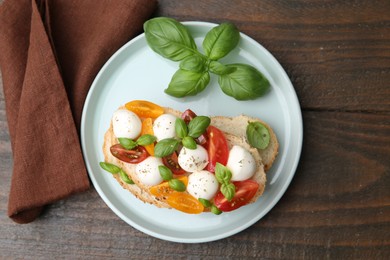 Photo of Tasty sandwich with mozzarella cheese, tomatoes and basil on wooden table, top view