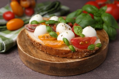 Photo of Tasty sandwich with mozzarella cheese, tomatoes and basil on brown table, closeup