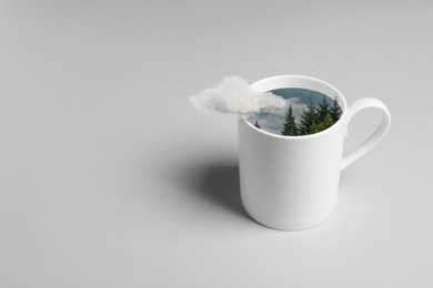 Image of Mountain forest in cup on grey background. Cloud flying out of cup