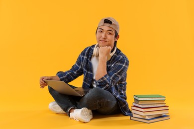 Photo of Student with headphones and laptop on orange background