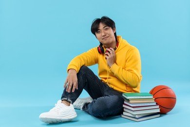 Photo of Student with books and basketball ball on light blue background