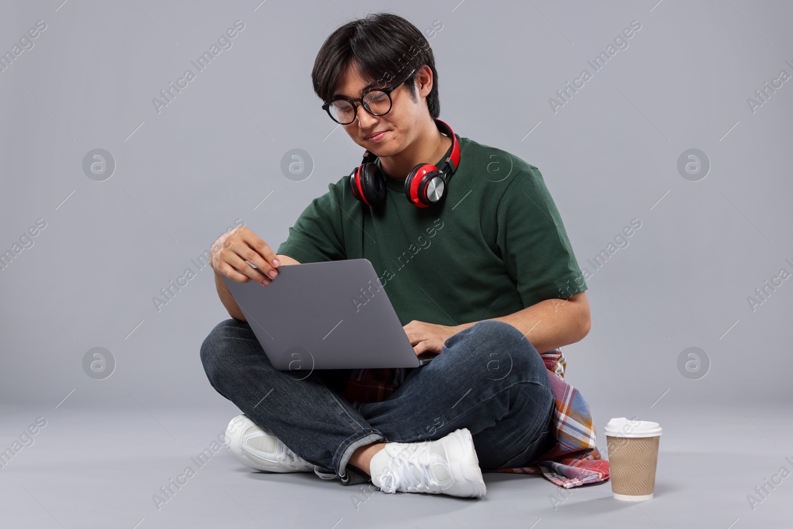 Photo of Student with headphones and laptop studying on grey background