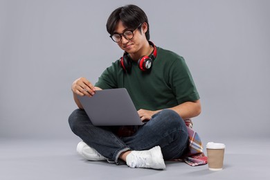 Photo of Student with headphones and laptop studying on grey background