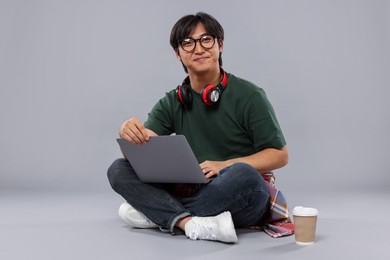 Photo of Student with headphones and laptop studying on grey background