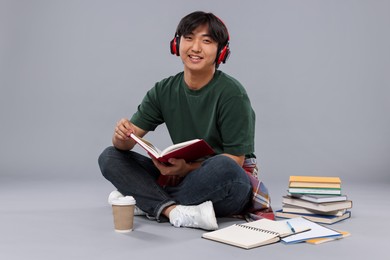 Photo of Student with headphones and book studying on grey background
