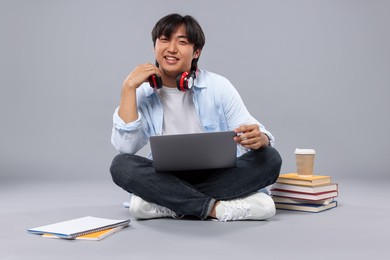 Photo of Student with headphones and laptop on grey background