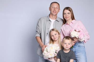 Photo of Family portrait of happy parents and their children with flowers on grey background. Space for text