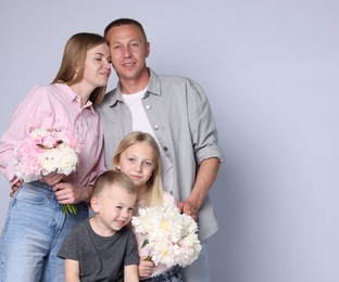 Photo of Family portrait of happy parents and their children with flowers on grey background. Space for text