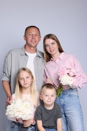 Photo of Family portrait of happy parents and their children with flowers on grey background