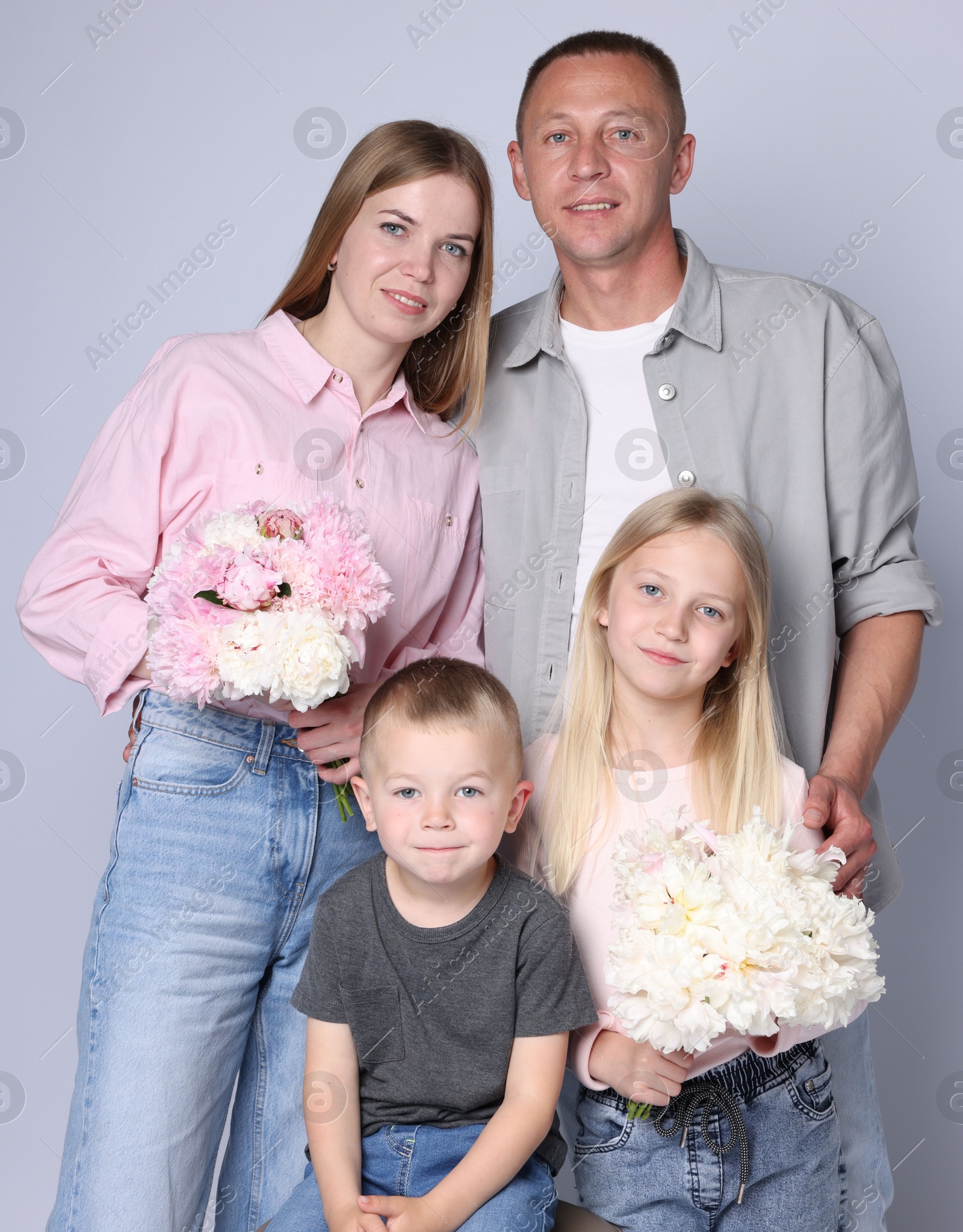 Photo of Family portrait of happy parents and their children with flowers on grey background
