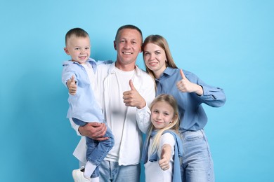 Photo of Family portrait of happy parents and their children showing thumbs up on light blue background
