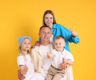 Photo of Family portrait of parents and their children showing thumbs up on yellow background